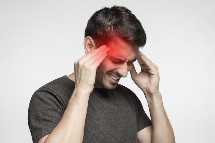 Closeup of young man touching temples with fingers as if suffering from severe migraine, feeling sick, isolated on gray background; Blog: Types of Headaches